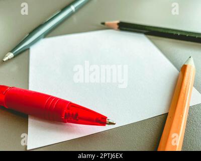 Schreibwaren auf dem Tisch im Büro. Zwei Stifte und Bleistifte zum Schreiben, eine Schreibmaschinenschere liegt auf Notizpapier. Kunststoffstifte mit Holzbleistiften. Stockfoto