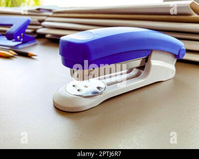 Bürobedarf für die Arbeit. Blauer Hefter zum Befestigen von Dokumenten. Schreibwaren im Büro auf dem Tisch. Der Hefter befindet sich neben Kartonordnern. Stockfoto