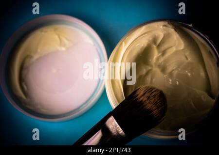 Eine Beauty-Box mit einer Holzbürste aus natürlichen harten Fusseln für einen Ton und ein rundes Glas Creme, eine Make-up-Basis mit einem zweiten Hauteffekt auf einem blauen B. Stockfoto