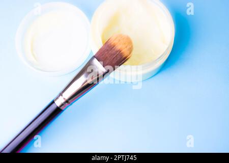 Eine Beauty-Box mit einer Holzbürste aus natürlichen harten Fusseln für einen Ton und ein rundes Glas Creme, eine Make-up-Basis mit einem zweiten Hauteffekt auf einem blauen B. Stockfoto
