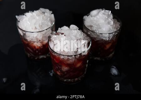 Alkoholischer Cocktail mit Eisnaht in altmodischen Gläsern auf schwarzem Betonhintergrund Stockfoto