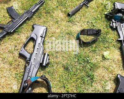 Schwarze Eisenmaschinengewehre der Armee, kleine Waffen für Soldaten mit Schalldämpfern liegen auf grünem Gras. Stockfoto