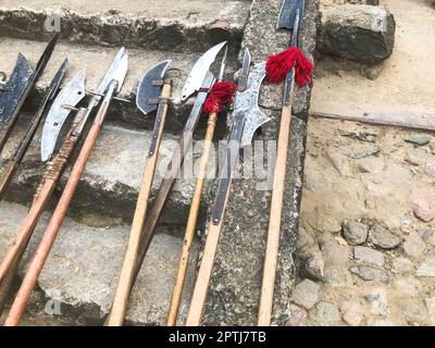 Die alten mittelalterlichen kalten Waffen, Äxte, Halberden, Messer, Schwerter mit Holzgriffen lecken auf den Steintreppen des Schlosses. Stockfoto