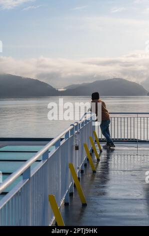 Unbekannter Tourist mit Fernglas bei Sonnenaufgang auf der Fähre der Inside Passage in der Nähe von Prince Rupert, British Columbia, Kanada. Stockfoto