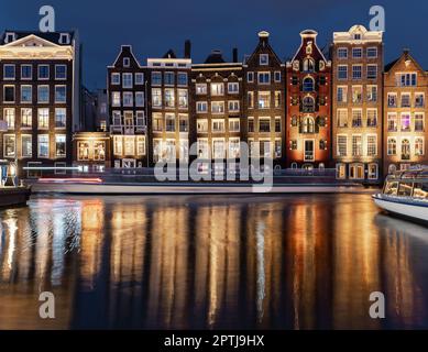 Tanzende Häuser Damrak Amsterdam während der Abendlichter Niederlande Holland. Atemberaubende schiefe, dünne Häuser, die zu Wahrzeichen von Amsterdam wurden, Stockfoto