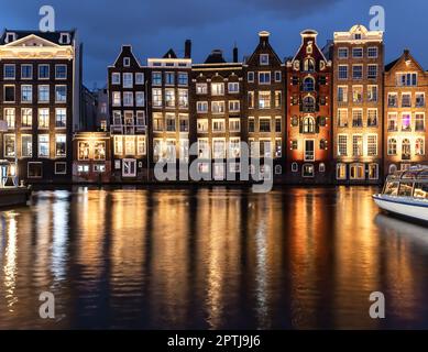 Tanzende Häuser Damrak Amsterdam während der Abendlichter Niederlande Holland. Atemberaubende schiefe, dünne Häuser, die zu Wahrzeichen von Amsterdam wurden, Stockfoto