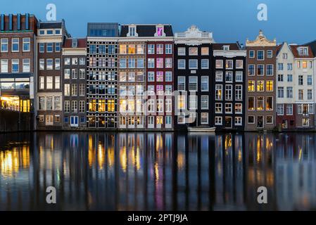 Tanzende Häuser Damrak Amsterdam während der Abendlichter Niederlande Holland. Atemberaubende schiefe, dünne Häuser, die zu Wahrzeichen von Amsterdam wurden, Stockfoto