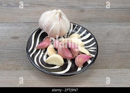 Frischer Knoblauchkopf mit geschälten und ungeschälten Knoblauchzehen in einer kleinen Keramikschüssel Stockfoto