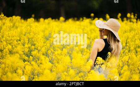 Ein hübsches blondes Mädchen posiert inmitten eines Feldes blühender gelber Rapsblumen Stockfoto