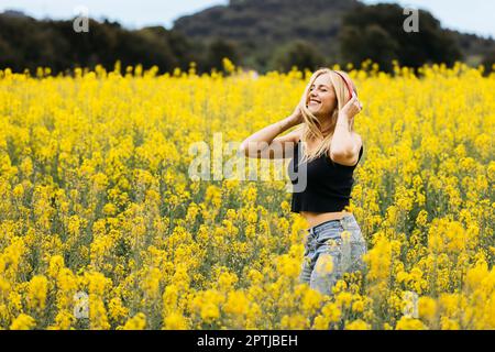 Ein hübsches blondes Mädchen posiert inmitten eines Feldes blühender gelber Rapsblumen Stockfoto