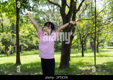 Portrait von Kind Mädchen hört Musik mit modernen Kopfhörern im Park im Freien. Fröhliches Kind, das mit Kopfhörern über den wi-Speed-Kopfhörer Rhythmen hört Stockfoto