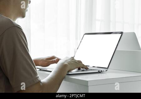 Die Hände eines Mannes, der zu Hause oder im Büro einen Laptop mit leerem Bildschirm auf einem weißen Tisch verwendet. Stockfoto