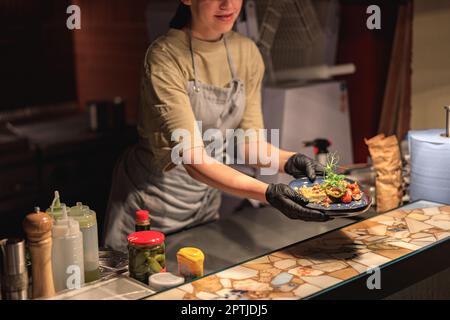 Nahaufnahme einer Chefkochin, die an der Bestellstelle in der offenen Restaurantküche Fertiggerichte serviert Stockfoto