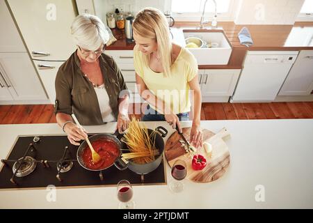 Es macht Spaß, deiner Tochter etwas Neues beizubringen. Eine Seniorin und ihre Tochter kochen in der Küche. Stockfoto