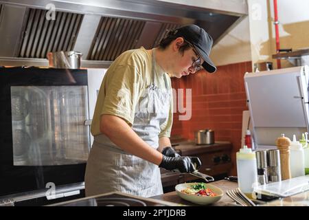 Professioneller Koch reißt Parmesan-Käse auf Fertiggerichten in der Restaurantküche Stockfoto