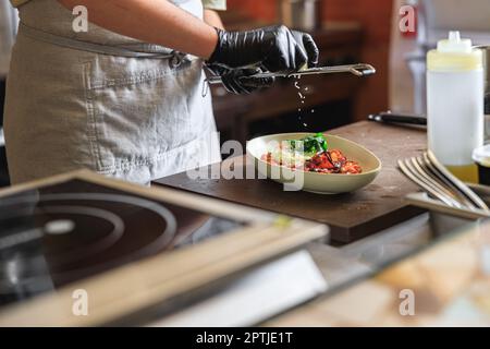 Professioneller Koch reißt Parmesan-Käse auf Fertiggerichten in der Restaurantküche Stockfoto