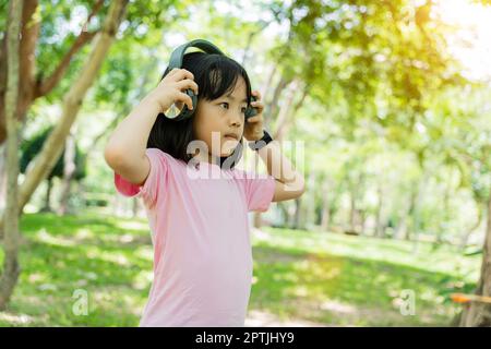 Porträt eines Mädchens, das Musik mit modernen Kopfhörern im Freien im grünen Park hört. Stockfoto