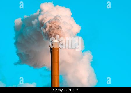 Verschmutzung durch einen Industriekamin, der eine große weiße und graue Rauchwolke in den Himmel bläst Stockfoto