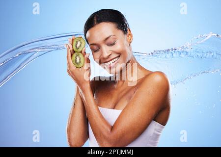 Hautpflege, Schönheit und Kiwi mit einem Wasserspritzer und schwarze Frau mit einem Lächeln auf blauem Studiohintergrund für Hydratation, Selbstpflege und Dermatologie. Glücklich Stockfoto