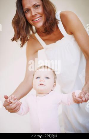 Babyschritte - sie ist fast bereit zu gehen. Porträt einer Mutter, die ihrer kleinen Tochter hilft, ihre ersten Schritte zu Unternehmen Stockfoto