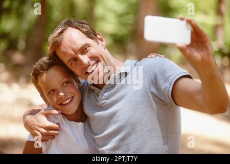 Erinnerungen halten ewig. Ein Vater und Sohn machen zusammen ein Selfie auf einem Campingausflug im Wald Stockfoto