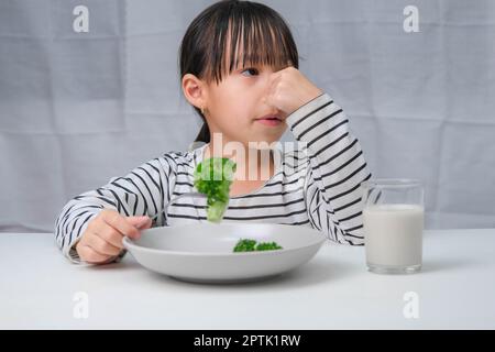 Kinder essen kein Gemüse. Süßes asiatisches Mädchen weigert sich, gesundes Gemüse zu essen. Ernährung und gesunde Ernährungsgewohnheiten für Kinder. Stockfoto