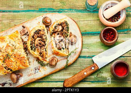 Geschlossener hausgemachter Pilzkuchen. In Scheiben geschnittener Champignonkuchen auf altem Küchenbrett Stockfoto