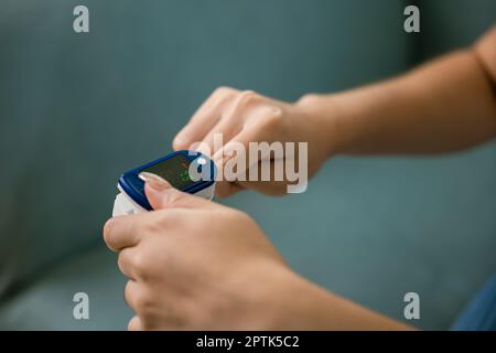 Junge Frau, die Pulsoxymeter verwendet, um Blut-Sauerstoffwerte und Pulsfrequenz am Finger unter dem Sofa im Wohnzimmer zu Hause zu überwachen, Self Healthcare mit coron Stockfoto