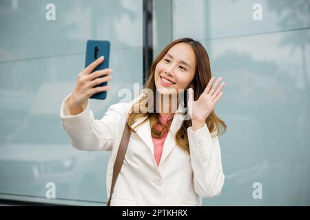 Glückliche Geschäftsfrau, die das Sonnenlicht im Freien genießt. Lifestyle und Technologie. Junge asiatische Geschäftsfrau während eines Videochats auf einem Smartphone o Stockfoto