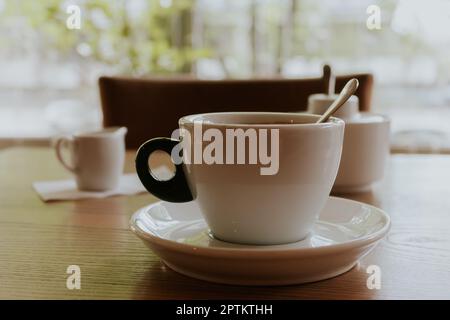 Eine Tasse Kaffee mit Milch. Morgenkaffee im Café. Im Café. Konzept für heiße Getränke. Espresso mit Milchsauce und Löffel. Zeit für einen Kaffee. Stockfoto