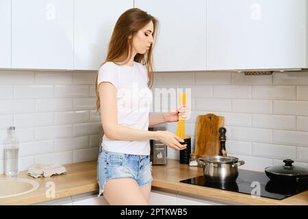 Junge, schöne Frau, die einen Haufen Spaghetti in der Hand hält. Die Hausfrau wird Nudeln in kochendes Wasser geben. Stockfoto