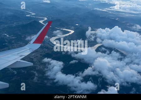 Flügel eines Flugzeugs, das über Wolken bedeckte Berggipfel fliegt. Blick auf die Hügel vom Flugzeug. Stockfoto