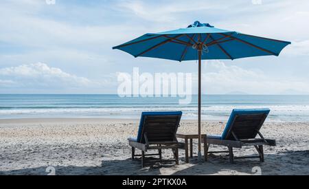 Liegestühle und Sonnenschirme am Sandstrand mit wolkenblauem Himmelshintergrund. Sommerurlaubsreisekonzept. Stockfoto