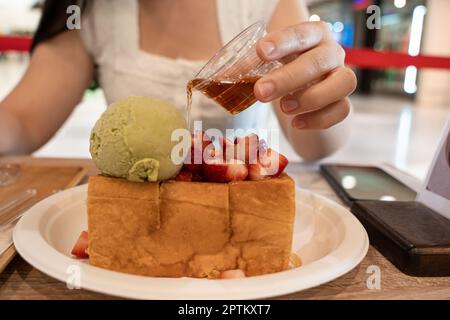 Nahaufnahme einer Frau, die Honig in leckeren Toast mit Erdbeeren auf dem Tisch gießt Stockfoto