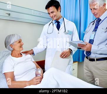 Wir haben alles unter Kontrolle. Zwei Ärzte, die einen älteren Patienten betreuen, der sich in einem Krankenhausbett befindet Stockfoto