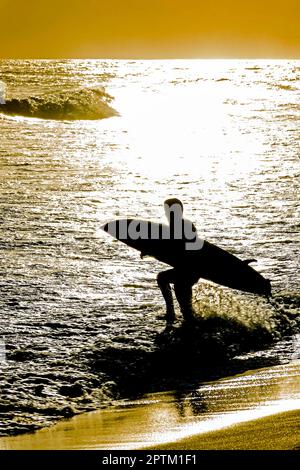 Silhouette eines Surfers, der das Meer mit seinem Surfbrett während des Sonnenuntergangs am Strand von Ipanema in Rio de Janeiro betritt Stockfoto