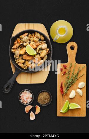 Gekochte Muscheln und Gewürze, bereit zum Frittieren auf schwarzem Hintergrund Stockfoto