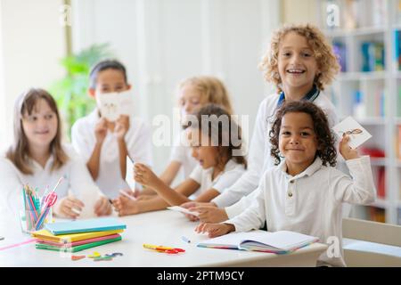 Die Kinder gehen zurück zur Schule. Interrassische Gruppe von Kindern unterschiedlichen Alters im Klassenzimmer. Die Schüler lernen lesen und schreiben. Vorschulkinder oder Kindergartenkinder mit Witz Stockfoto