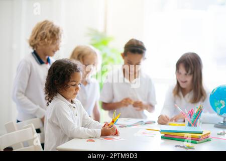 Die Kinder gehen zurück zur Schule. Interrassische Gruppe von Kindern unterschiedlichen Alters im Klassenzimmer. Die Schüler lernen lesen und schreiben. Vorschulkinder oder Kindergartenkinder mit Witz Stockfoto