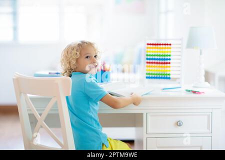 Kind macht Hausaufgaben zu Hause. Kleiner Junge mit bunten Holzabakus, der Mathematik macht und zusätzlich lernt und zählt. Kinder lernen und lernen. Stockfoto