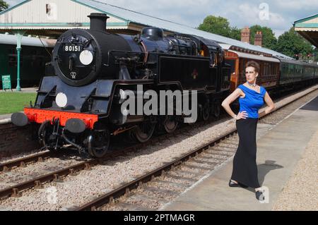 Gesamtporträt einer Frau mit 1957 BR Standard Class 4MT Panzerlokomotive am Horsted Keynes Bahnhof, West Sussex, Großbritannien. Modell: Der Universelle Appell. Stockfoto