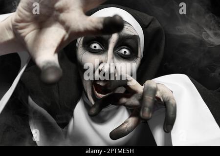 Gruselige, teuflische Nonne, die vor schwarzem Hintergrund Angst hat. Halloween-Party-Look Stockfoto