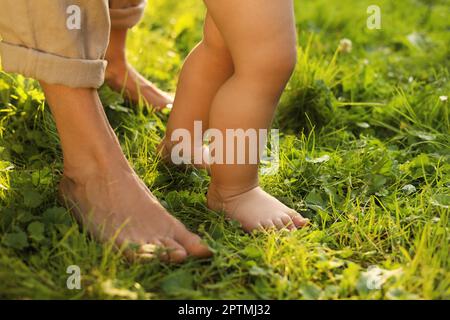 Eine Frau mit ihrem Kind, die barfuß auf grünem Gras im Freien läuft, Nahaufnahme Stockfoto