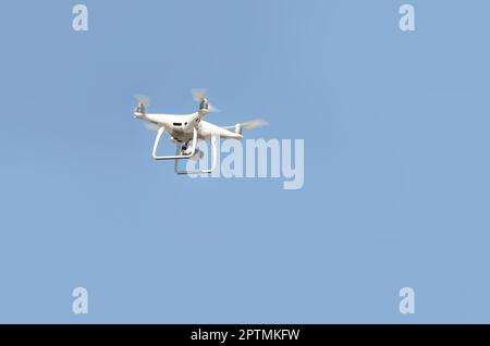 Big White drone schwebt in einem hellen wolkenlosen blauen Himmel, Radio Control Helicopter mit tragbaren Videokamera Versorgung Stockfoto
