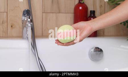 Eine Frau, die eine Badebombe über der Badewanne hält, drinnen, Nahaufnahme Stockfoto