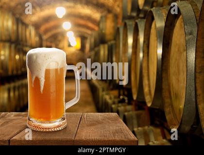 Ein Glas leckeres Bier auf einem Holztisch im Keller mit großen Fässern, Platz für Text Stockfoto