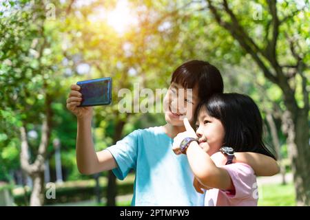 Zwei Schwestern umarmen sich, während sie im Park Selfie mit dem mobilen Smartphone machen. Happy Friendship Familienkonzept. Stockfoto