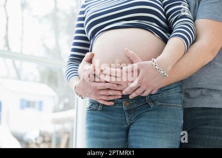 Der mittlere Teil des Mannes hält den Bauch seiner schwangeren Frau Stockfoto