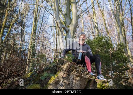 Fit für einen jungen Mann, der sich auf einem Baumstumpf im Wald entspannt Stockfoto