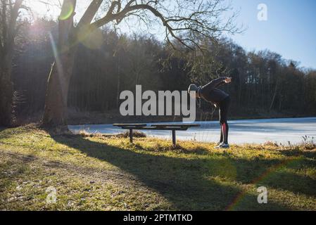 Ein junger Mann, der sich auf dem Fitness Trail am gefrorenen See streckt Stockfoto
